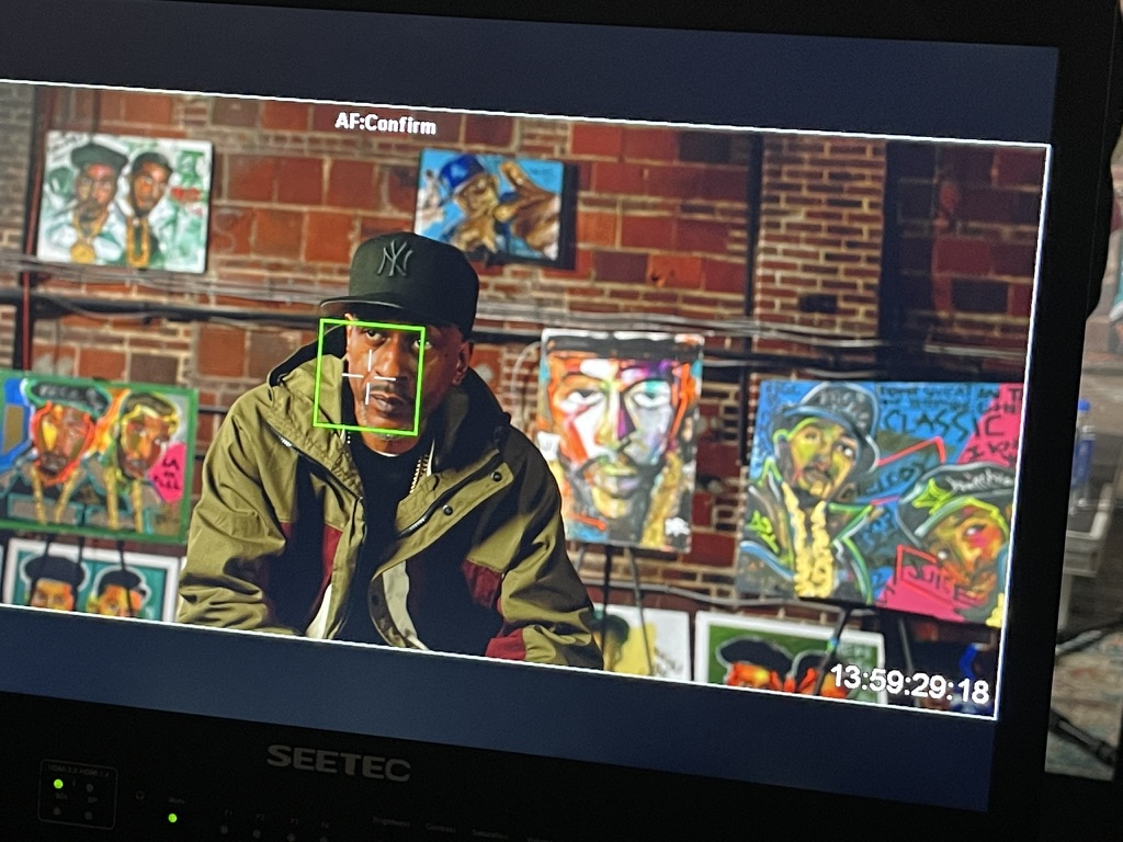 Interview framed up on the monitor in front of a wall of portraits